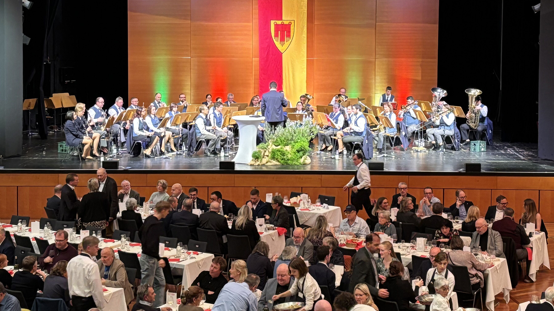 Menschen in der Kongresshalle beim Essen und eine Musikkapelle auf er Bühne