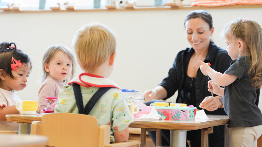 Kita-Mitarbeiterin mit Kindern am Tisch