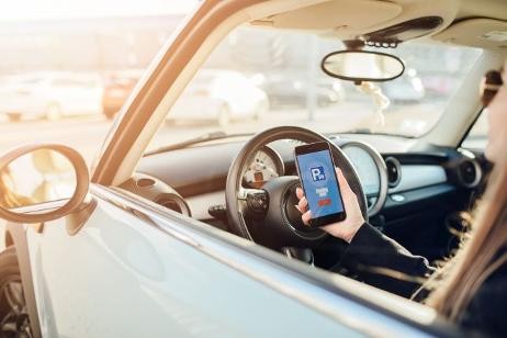 Frau im Auto mit Handy und Parkgebühren App